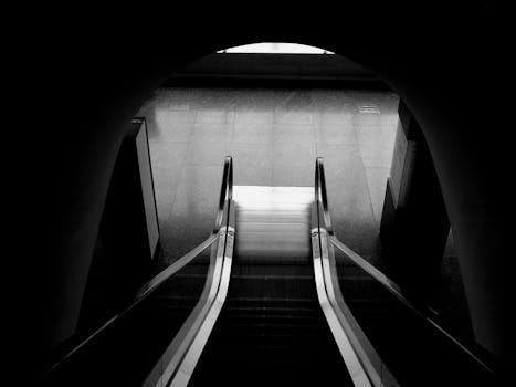 A high angle black and white view of a modern escalator leading downward, emphasizing architecture.